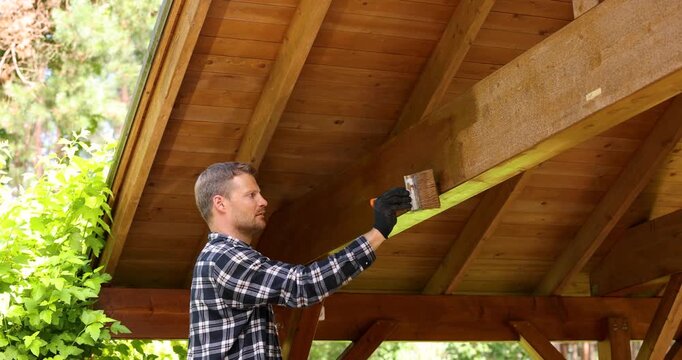 man painting timber frame outdoor carport with paintbrush and wood protective paint