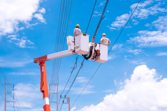 Two electricians on bucket boom truck are connecting electrical cable lines against blue sky background, low angle view with copy space
