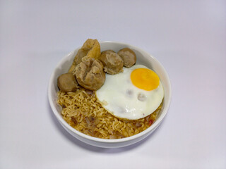 Single serving of food in a white bowl with seasoned noodles, generously topped with round meatballs, pieces of fried tofu, sunny-side-up fried egg. Related to Asian cuisine, home cooking, fast food