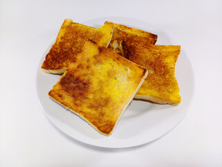 A pile of evenly toasted, golden-brown bread slices, buttered and sugared, on a white plate, against a white background. Related to breakfast food, sweet snacks, comfort food, culinary delights