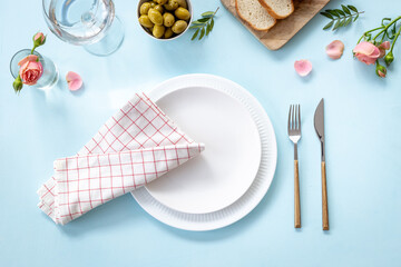Festive table setting with empty plate, cutlery and napkin - flowers decorated, bread and olives for dinner, flat lay. Top view