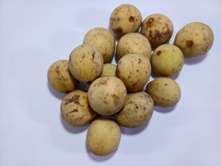 A cluster of perfectly ripe duku fruits, with distinctive light brown, oval-shaped skins, is artfully arranged on a pristine white surface. Their smooth, unblemished surfaces suggest sweet and juicy