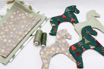 Christmas tree toys made by hand. On a flat surface beautiful cotton fabric with a New Year's ornament, handmade horses and threads. White background.