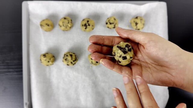 Placing chocolate chip cookie dough ball on baking tray with parchment paper for homemade dessert preparation &mdash; step-by-step cooking tutorial for recipe and food content