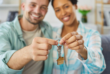 Happy smiling young couple holding house keys in hands sitting in living room at home looking at camera enjoying real estate purchase celebrating moving day. Relocating, mortgage concept.