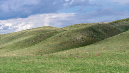 Fototapeta premium Long mountains. Rolling green hills under a cloudy sky, showcasing the beauty of nature with vibrant grass and gentle slopes, creating a serene and peaceful landscape scene