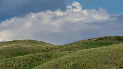 Naklejka premium Long mountains. Rolling green hills under a dramatic sky filled with clouds, showcasing the beauty of nature and the tranquility of the landscape in a serene environment