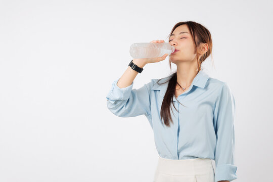 Closed eyes, young asian woman hold plastic bottle to drink, enjoying refreshing water, she is hydrated; drink water is part of a healthy lifestyle, isolated studio white background