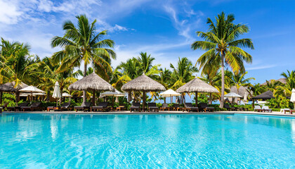 Stunning wide view of turquoise tropical resort swimming pool with crystal-clear water sparkling under bright midday sun and palm trees