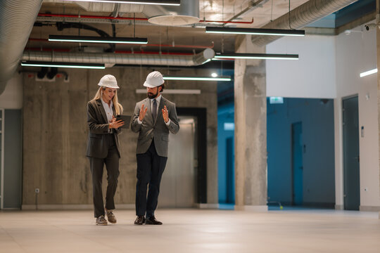 Architects walking and discussing in empty office using tablet - Powered by Adobe