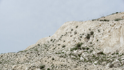 Pokrovsky Cretaceous mountains. White rocky hillside with sparse vegetation under a cloudy sky, showcasing natural textures and geological formations in a serene outdoor environment