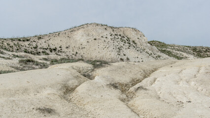 Pokrovsky Cretaceous mountains. Natural landscape featuring sandy hills and sparse vegetation under a cloudy sky, showcasing the beauty of arid terrain and unique geological formations