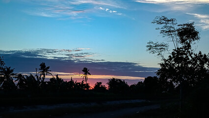 A bright morning, the sun is rising. A clear blue sky. Orange hues in the distance. A silhouette photo.