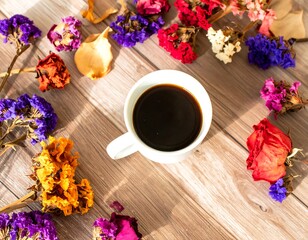 Coffee cup surrounded by dried flowers on wooden table