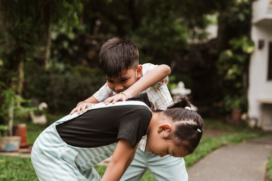 Two Filipino children playing Luksong Baka in a garden setting, enjoying a traditional and energetic outdoor activity together.