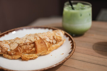 A freshly baked croissant, topped with almond petals, and an iced matcha latte on a garden table.