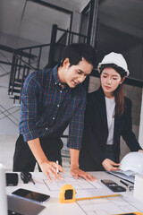 Construction manager and engineer dressed in orange work vests and hard helmets explore construction documentation on the building site near the steel frames