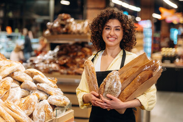 Female worker in apron is with bakery in hands, standing in the supermarket