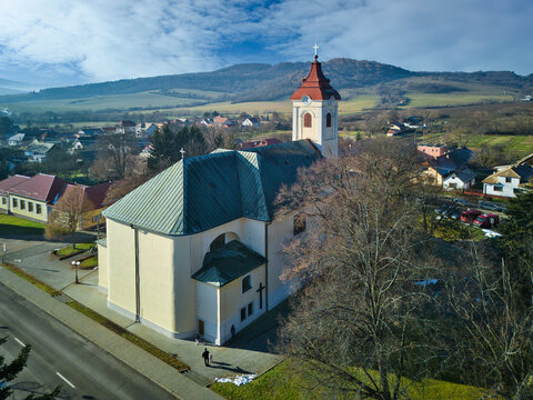 Aerial view of a church with a red-roofed tower, standing prominently amidst the town's architecture against a backdrop of rolling hills, Detva, Bansk&Atilde;&iexcl; Bystrica Region, Slovakia.