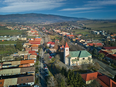 Aerial view of a vibrant church with red towers stands prominently amid the town's terracotta rooftops, contrasted against the backdrop of distant mountains, Detva, Bansk&Atilde;&iexcl; Bystrica Region, Slovakia.
