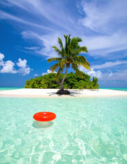 Beautiful tropical island with single palm tree on white sandy beach surrounded by turquoise ocean and vibrant red inflatable float under sunny blue sky