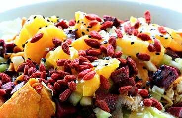 closeup of Kumara salad plate. selective focus. appetizing fresh food. ice lettuce, orange cubes, chicken breast slices, red beats, red goji seeds, celery bits, black sesame seeds. healthy eating