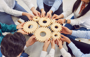 Top view shot of a diverse team of people holding wooden gears, cogwheel in a circle. Their hands are working together, symbolizing teamwork and group collaboration in achieving common goals.