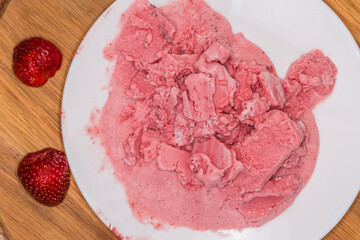 Melted strawberry ice cream on dish, fresh strawberries, top view