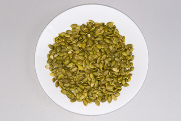 Peeled pumpkin seeds on dish on gray surface, top view