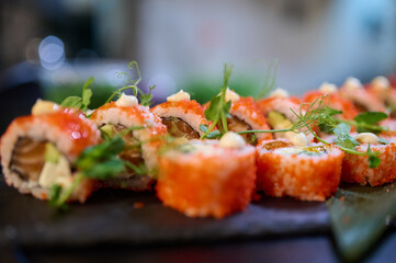 Close-up of delicious sushi rolls topped with tobiko, cream sauce, and microgreens, arranged on a black slate plate in a Japanese restaurant