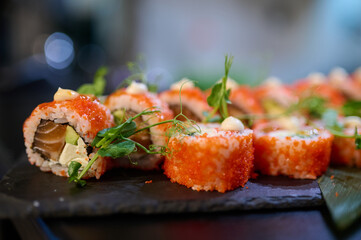 Close-up of delicious sushi rolls topped with tobiko, cream sauce, and microgreens, arranged on a black slate plate in a Japanese restaurant