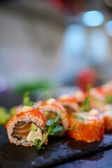 Close-up of delicious sushi rolls topped with tobiko, cream sauce, and microgreens, arranged on a black slate plate in a Japanese restaurant