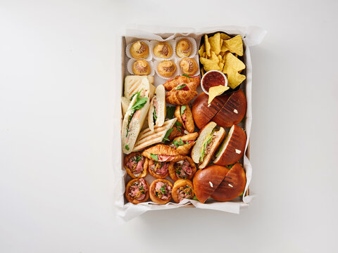 An abundant variety of snacks is arranged in a box, featuring sandwiches, pastries, and chips. This spread is perfect for any gathering or celebration, showcasing colorful and enticing options