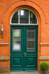 old wooden door. Above the doors, a large transom window with stained or textured glass is set beneath a brick archway. An old-fashioned lantern hangs above the door
