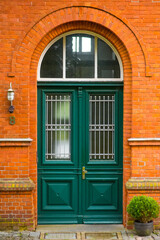 old wooden door, Above the doors, a large transom window with stained or textured glass is set beneath a brick archway. An old-fashioned lantern hangs above the door