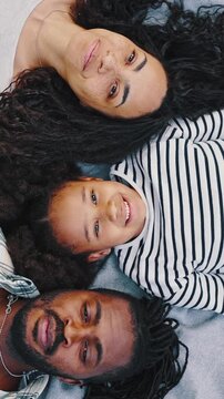 Top view of Happy African family resting and having fun on picnic in city park, enjoying and lying on a plaid in meadow, on green grass. Parents and child looking up at camera