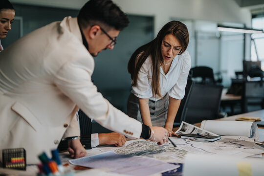A diverse team collaborates on architectural plans in a modern office setting. The group is actively engaged in discussing blueprints, showcasing teamwork and project management skills.