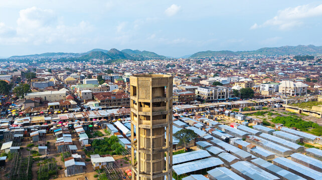 Aerial view of a solitary tower rising above the bustling market and cityscape, the distant hills adding depth to the horizon, Jos, Plateau, Nigeria.