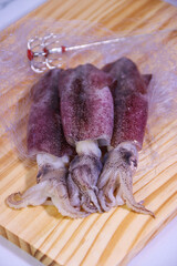 Three Squids on Wooden Cutting Board with Partial Net, Vertical Arrangement