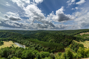 Obraz premium Panoramic view of lush green forest with rolling hills and winding river. Vibrant blue sky with fluffy clouds creating picturesque landscape. Top site in Ardennes region, Wallonia, Belgium.