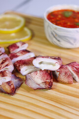Grilled Squid Pieces on Wooden Board with Dipping Sauce and Lime Wedges