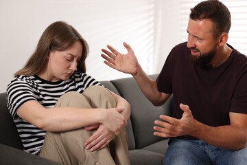 Betrayal. Angry man shouting at his frustrated wife on sofa at home