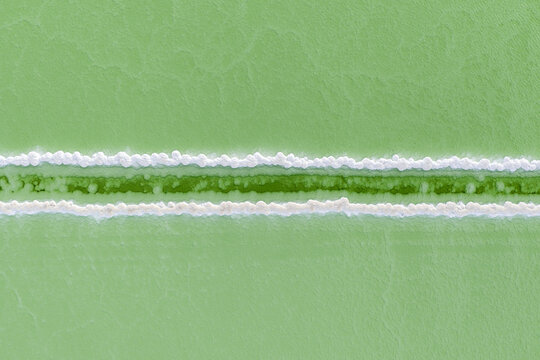 Aerial view of striking bands of white salt crystals contrast with the surrounding pale green waters of Lake Chaerhan, Lake Chaerhan, Qinghai, China.