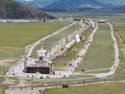 Aerial view of the expansive Bage Mani Stone Wall stretching across the landscape, a tapestry of green fields and distant mountains, Bage Mani Stone Wall, Sichuan, China.