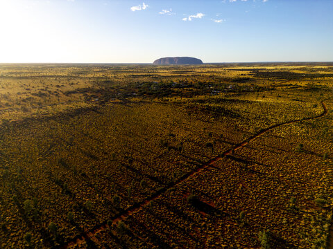 Aerial view of the iconic monolith of Uluru rises majestically from the ochre-red desert floor under the vast, azure sky, Petermann, Northern Territory, Australia.
