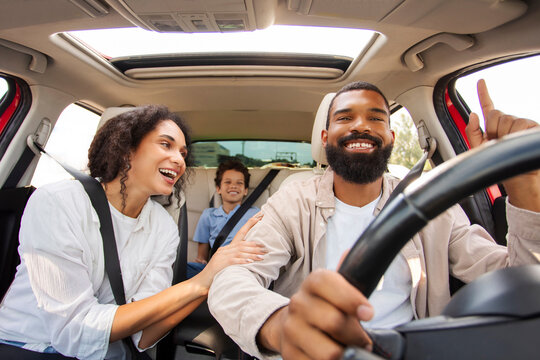 Overjoyed Latin parents and son driving car, chatting and laughing, family going on vacation, windshield view