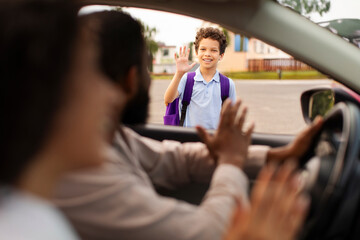 Parents bringing their son to school, sitting in car and waving goodbye to child boy, view from...