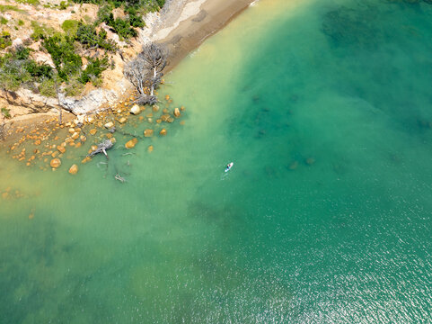 Aerial view of the golden-toned cliffs meeting the turquoise sea near 95 Deerys Road, a lone paddleboarder gliding through the serene waters, &Aring;&OElig;rere Point, Auckland, New Zealand.