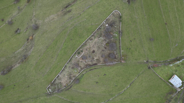 Aerial view of a triangular walled structure stands stark against the vibrant green pasture, a silent sentinel in the rolling landscape, Posof, Ardahan, T&Atilde;&frac14;rkiye.