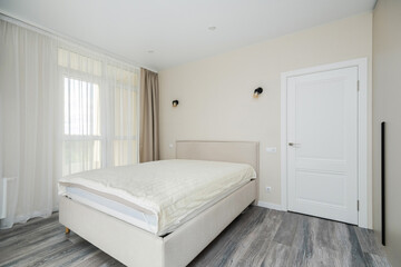 Modern bedroom with neutral tones and natural light from large windows